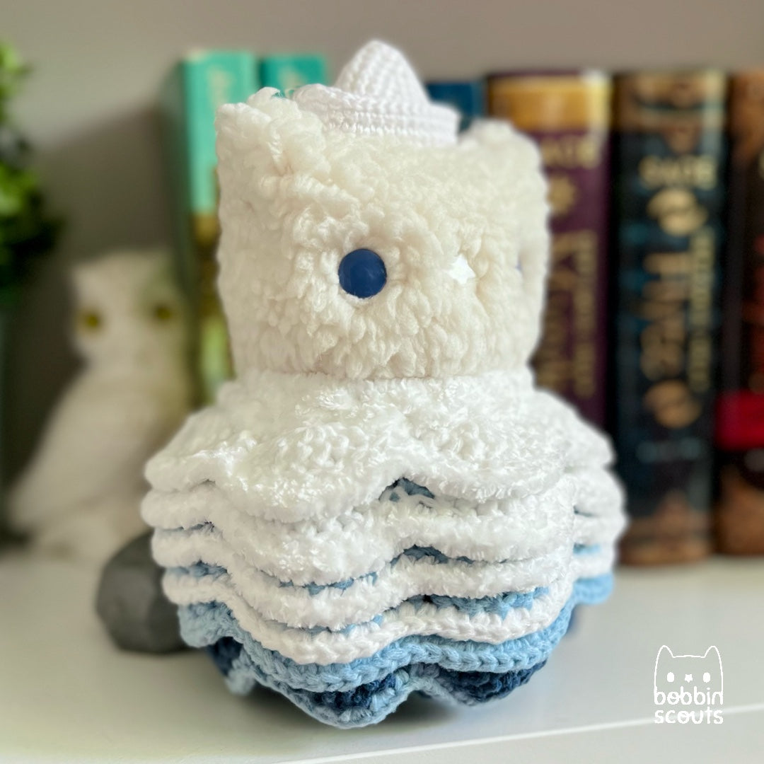 cream plushie with a crocheted shell made to look like ocean waves and a tiny sailboat on its head