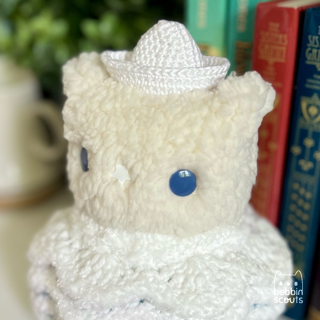 cream plushie with a crocheted shell made to look like ocean waves and a tiny sailboat on its head